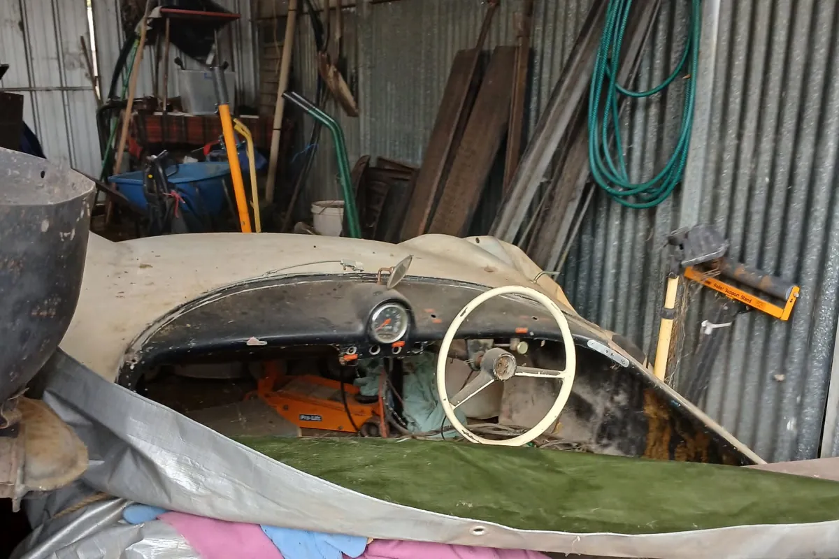 c1960 Goggomobil Dart project car in a shed, showing the cream fibreglass body, dash and steering wheel, partly under covers