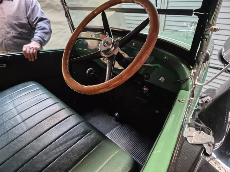 Cockpit of the c1928 Chevrolet Roadster showing the timber-rimmed steering wheel, green dashboard and black leather bench seat