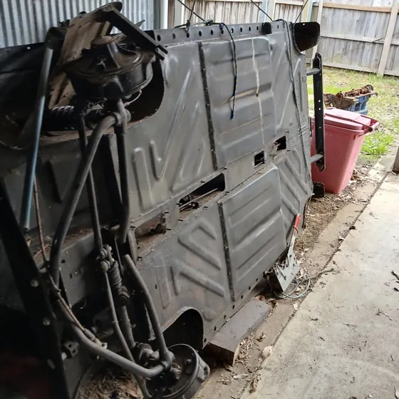 Floorpan and running gear of the c1960 Goggomobil Dart standing on end in a shed, showing the suspension and brake lines